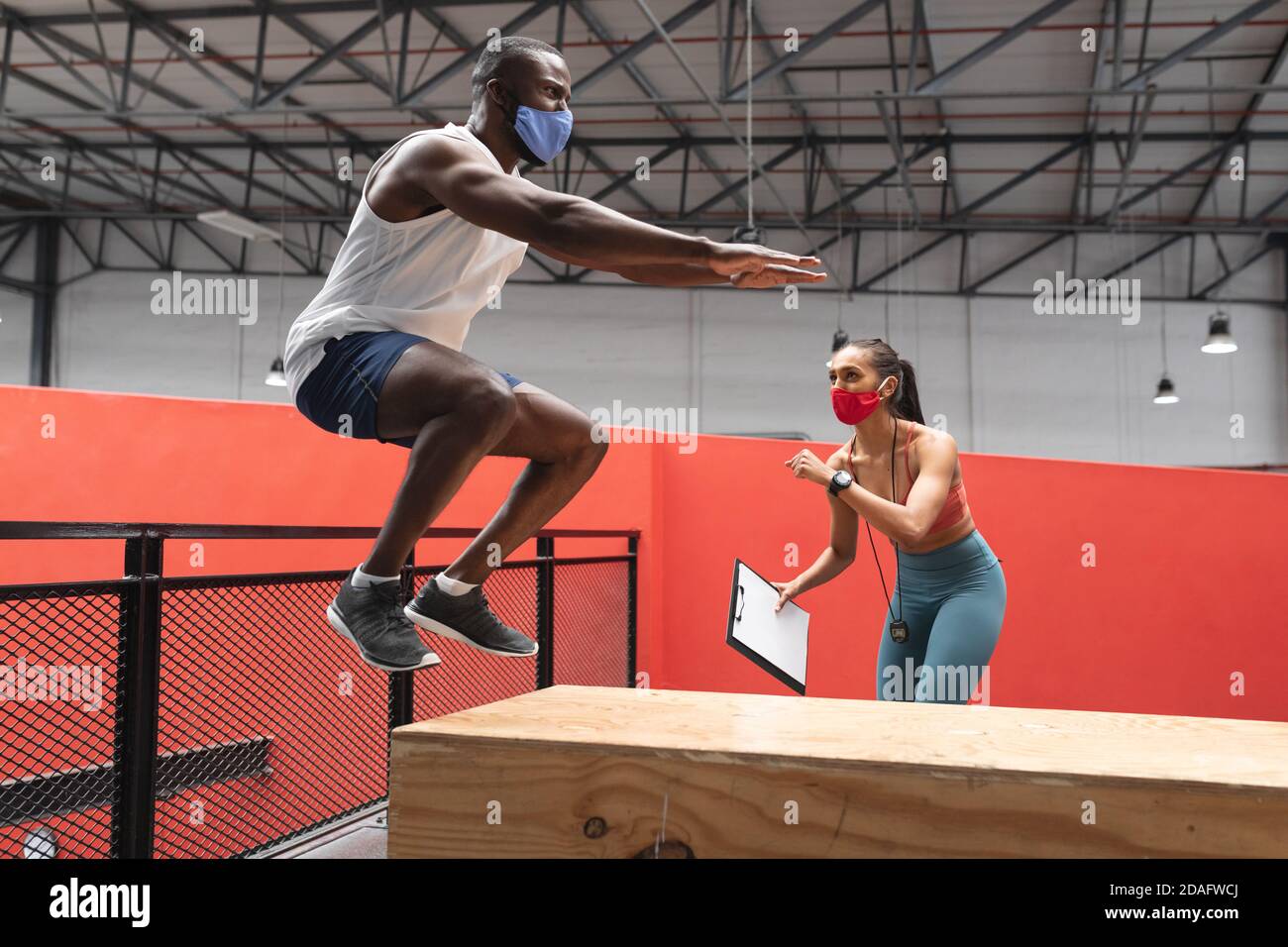 Fit afroamerikanischen Mann trägt Gesichtsmaske Springen auf Holz plyo-Box im Fitnessstudio, während kaukasische f Stockfoto