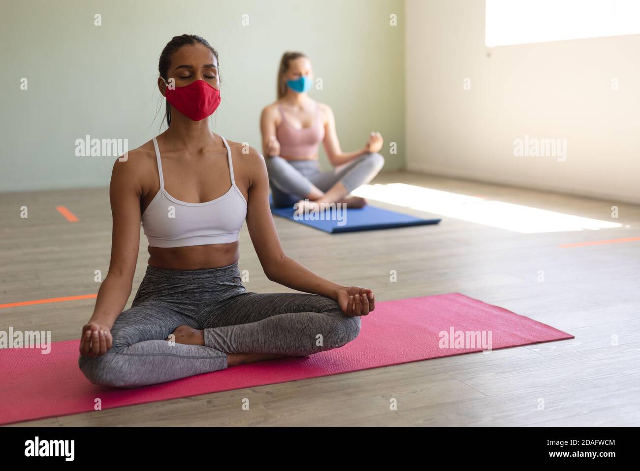 Zwei fit kaukasische Frau trägt Gesichtsmasken üben Yoga während Sitzen auf Yogamatten im Fitnessstudio Stockfoto