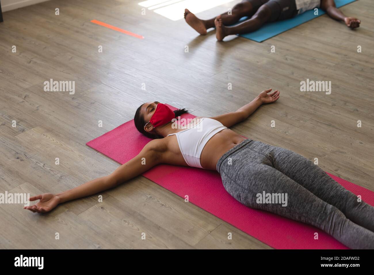 Fit Frau kaukasischen trägt Gesichtsmaske Yoga üben während liegen Auf Yogamatten im Fitnessstudio Stockfoto