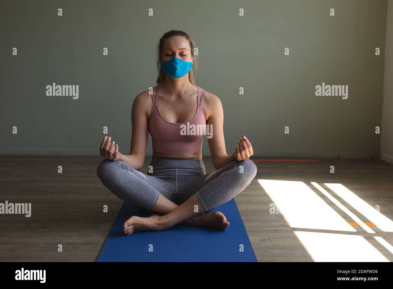 Fit kaukasische Frau trägt Gesichtsmaske Yoga üben während des Sitzens Auf Yogamatte im Fitnessstudio Stockfoto