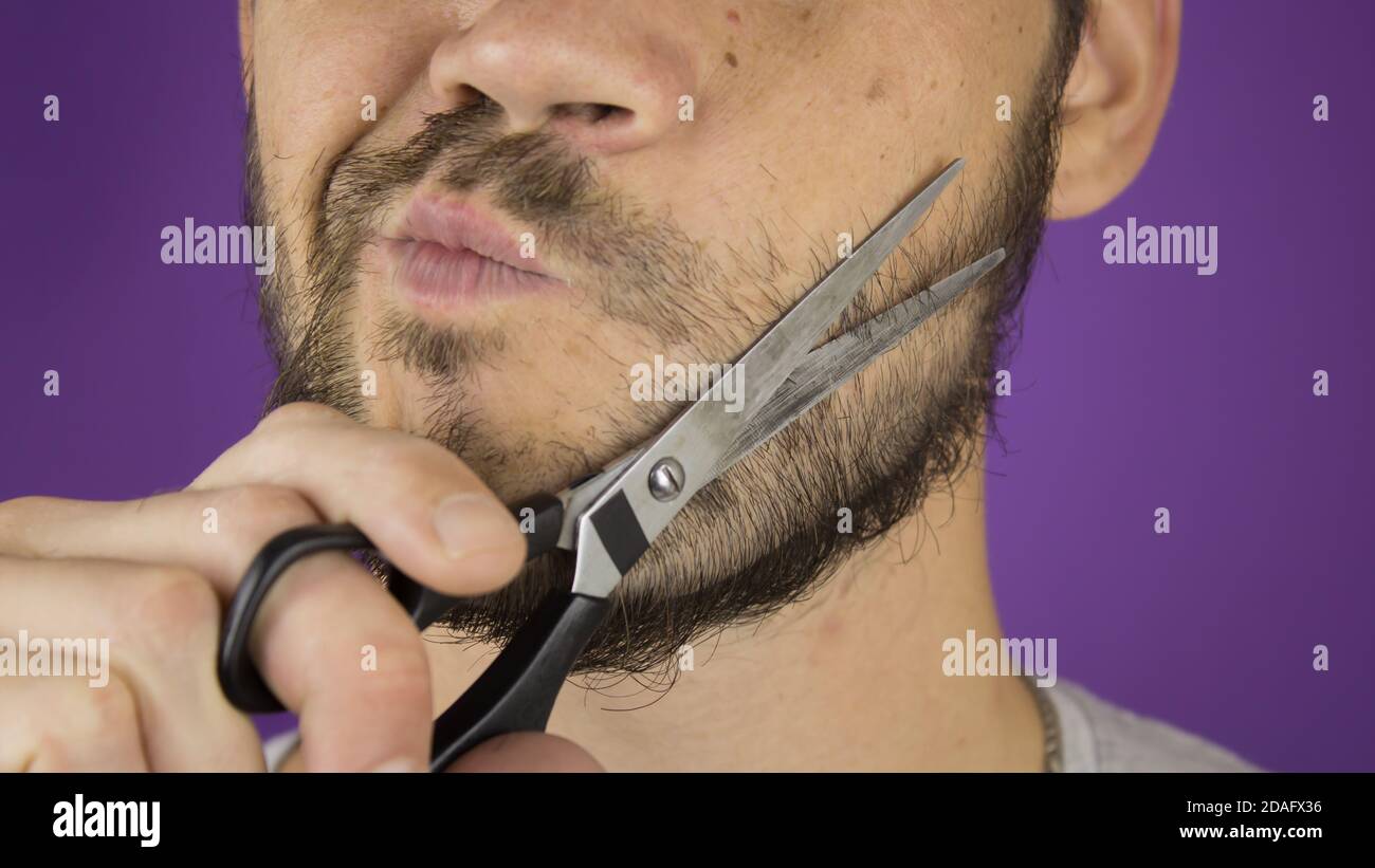 Schöner junger Kerl trimmt seinen Bart mit einer Schere. Stockfoto