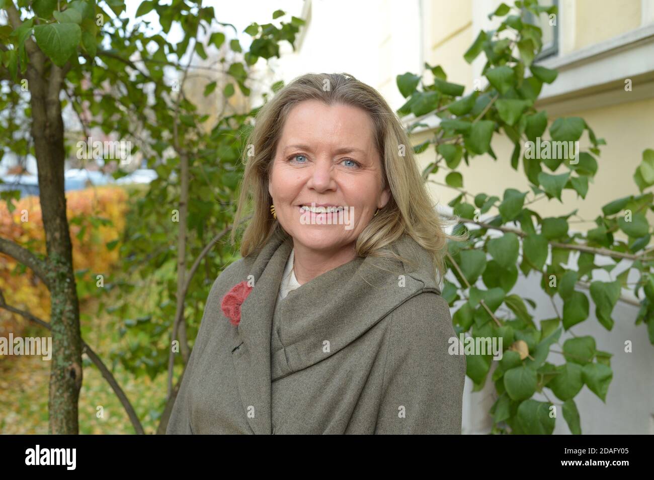 Frau mit intensiven blauen Augen mit einem grauen Mantel im Freien In einem städtischen und grünen Bereich Stockfoto