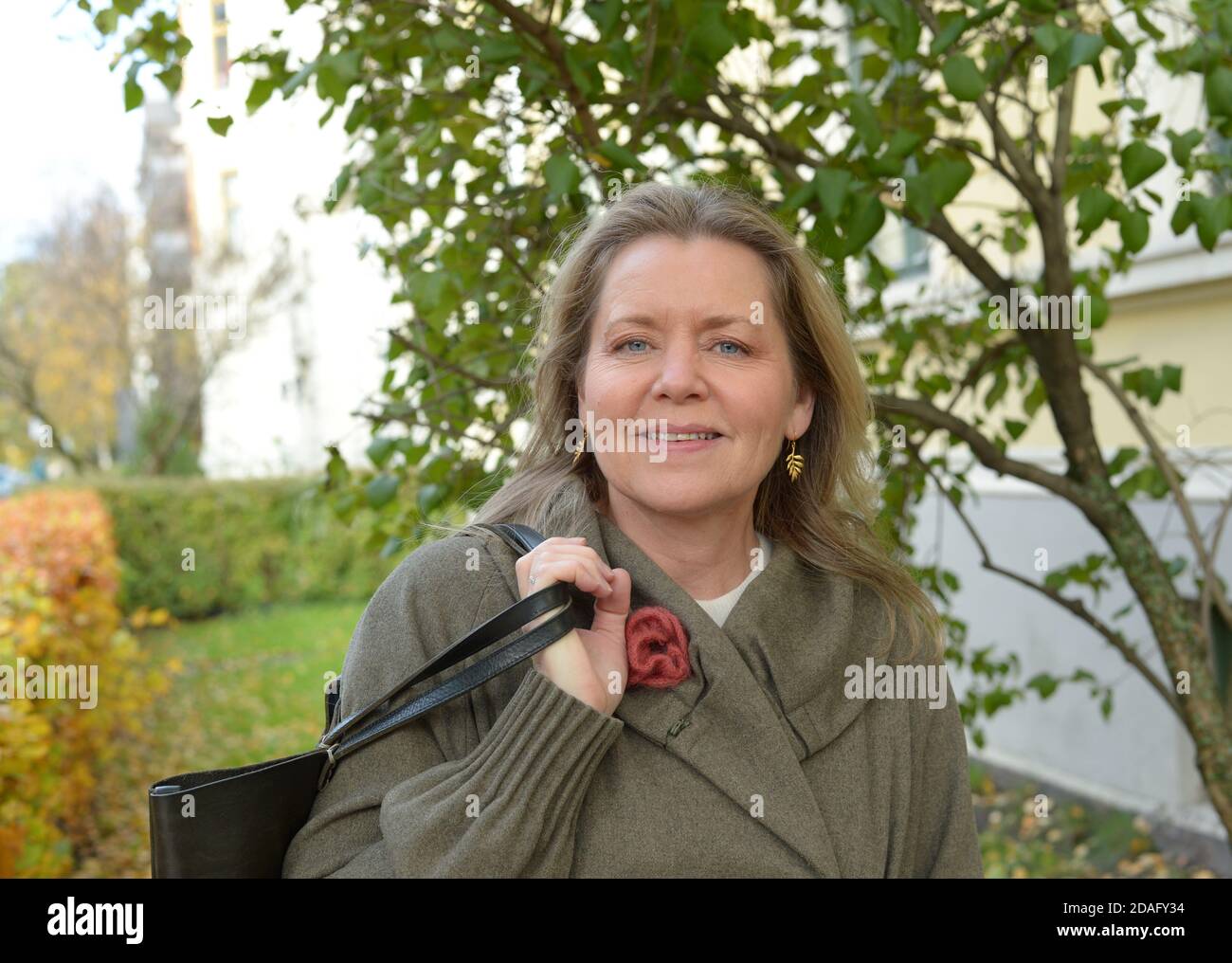 Frau mit intensiven blauen Augen mit einem grauen Mantel im Freien In einem städtischen und grünen Bereich Stockfoto