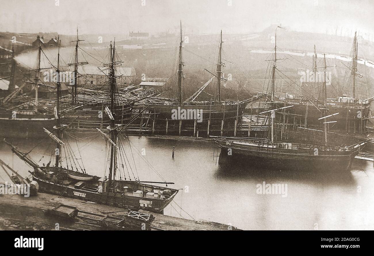 Ein seltenes und ungewöhnliches altes Foto, das Segelschiffe zeigt, die in der Whitehall-Werft am Fluss Esk in Whitby, North Yorkshire (UK) während der viktorianischen Zeit gebaut oder repariert wurden. White Hall oder Whitehall (noch im Jahr 2020) war die Heimat des Werftbesitzers Thomas Turbull. Die beiden Giegelenden des Gebäudes (oben links) sind im Bild zu sehen. Auf der anderen Flussseite liegt ein Kollier, der Kohle an die Öffentlichkeit verkauft, in der Nähe des Parkplatzes und der Marina des Co-op-Geschäfts (2020). Stockfoto