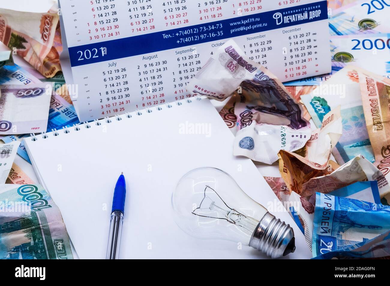 Glühbirne und Kalender, Lampe und Geld, zerknittertes Geld und Notepad, zerknittertes russisches Geld Stockfoto