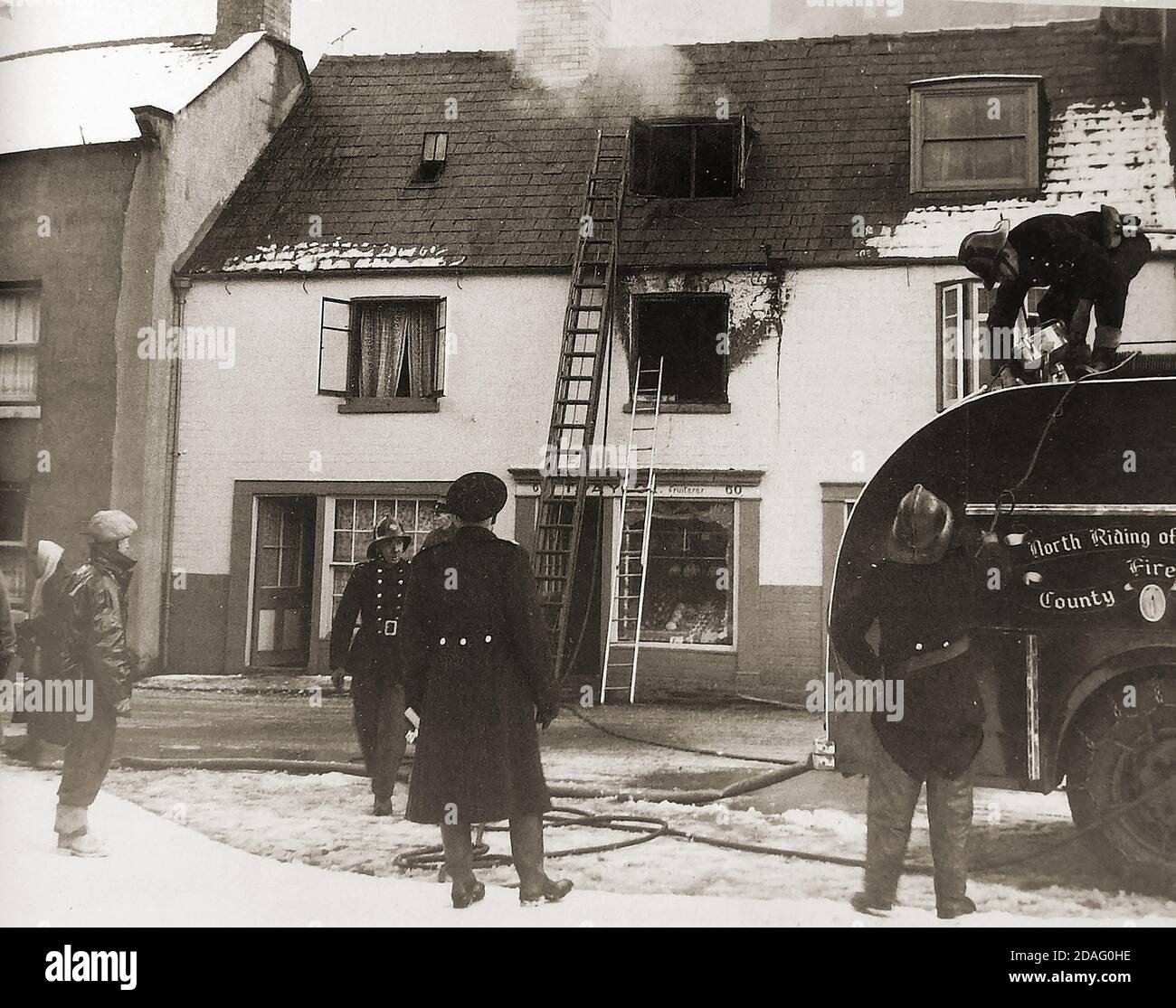 Ein Vintage-Foto, das eine Feuerwehr von North Riding of Yorkshire (UK) zeigt, die einen Brand über Paylors Obstgeschäft, Church Street, Whitby, North Yorkshire, mit Schnee auf dem Boden bekämpft. Stockfoto