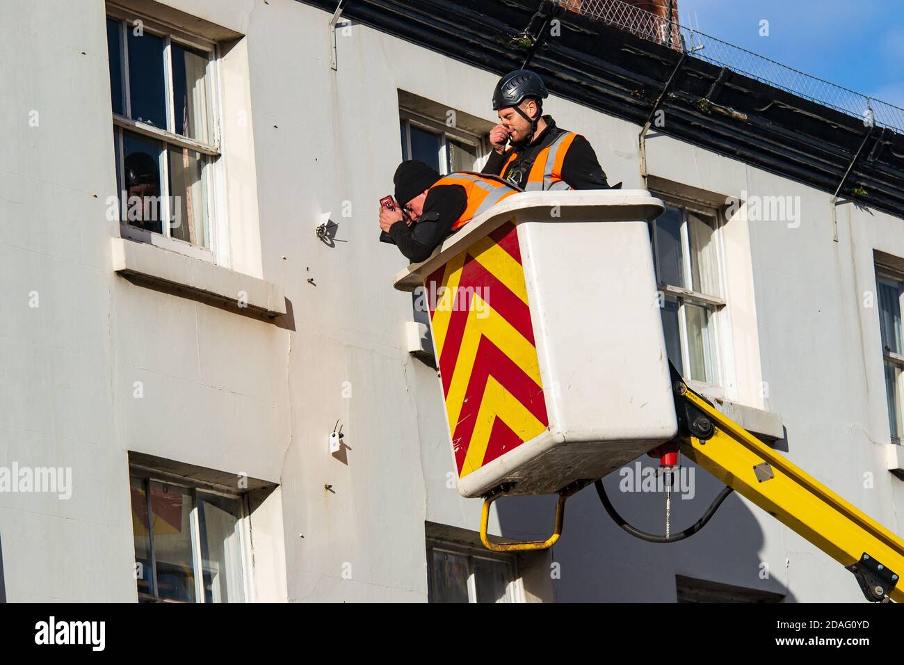 Zwei Männer, die in der Höhe in einem Kirschpflücker arbeiten und an einer weißen Hausfront arbeiten. Stockfoto