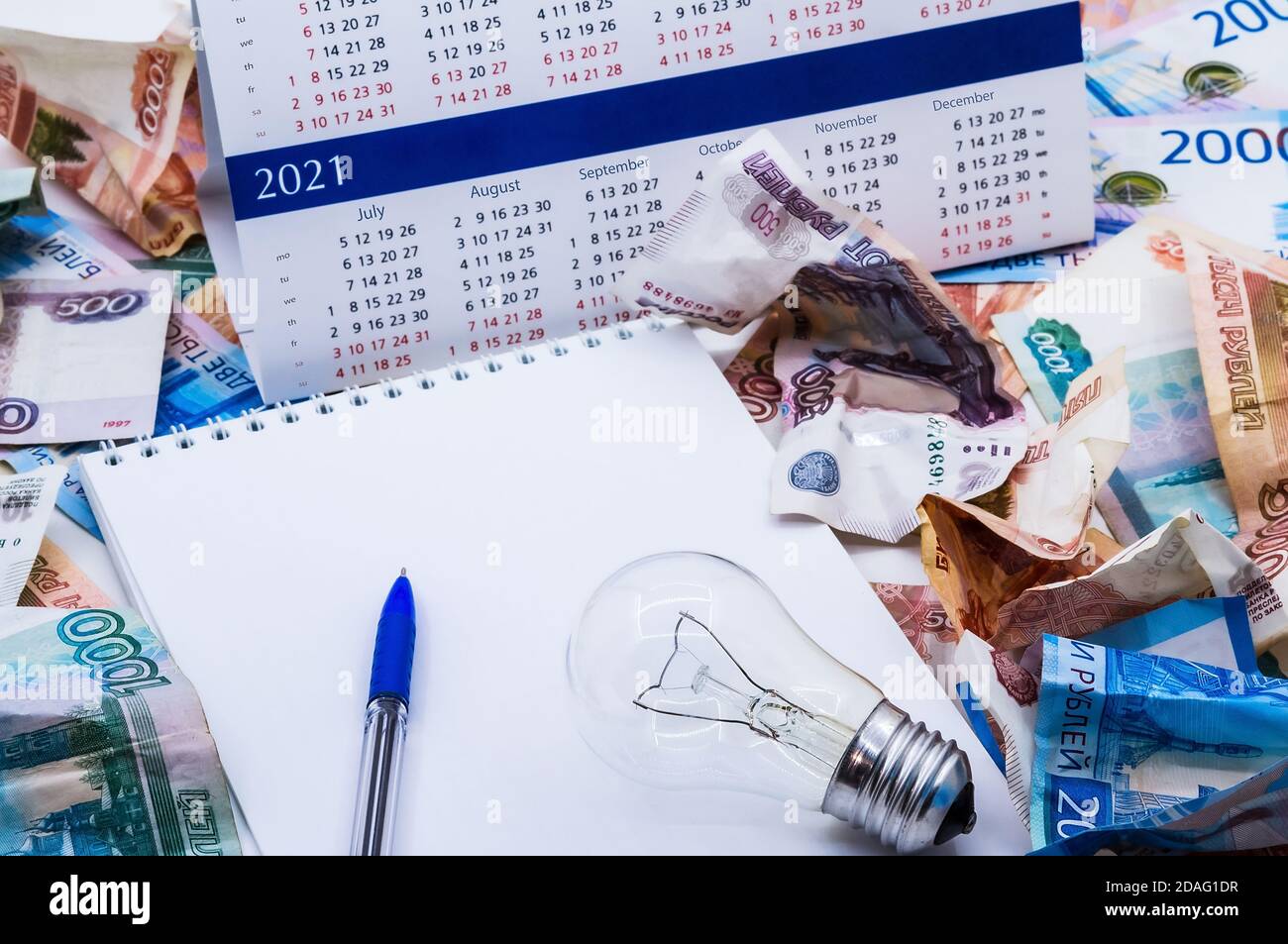 Glühbirne und Kalender, Lampe und Geld, zerknittertes Geld und Notepad, zerknittertes russisches Geld Stockfoto