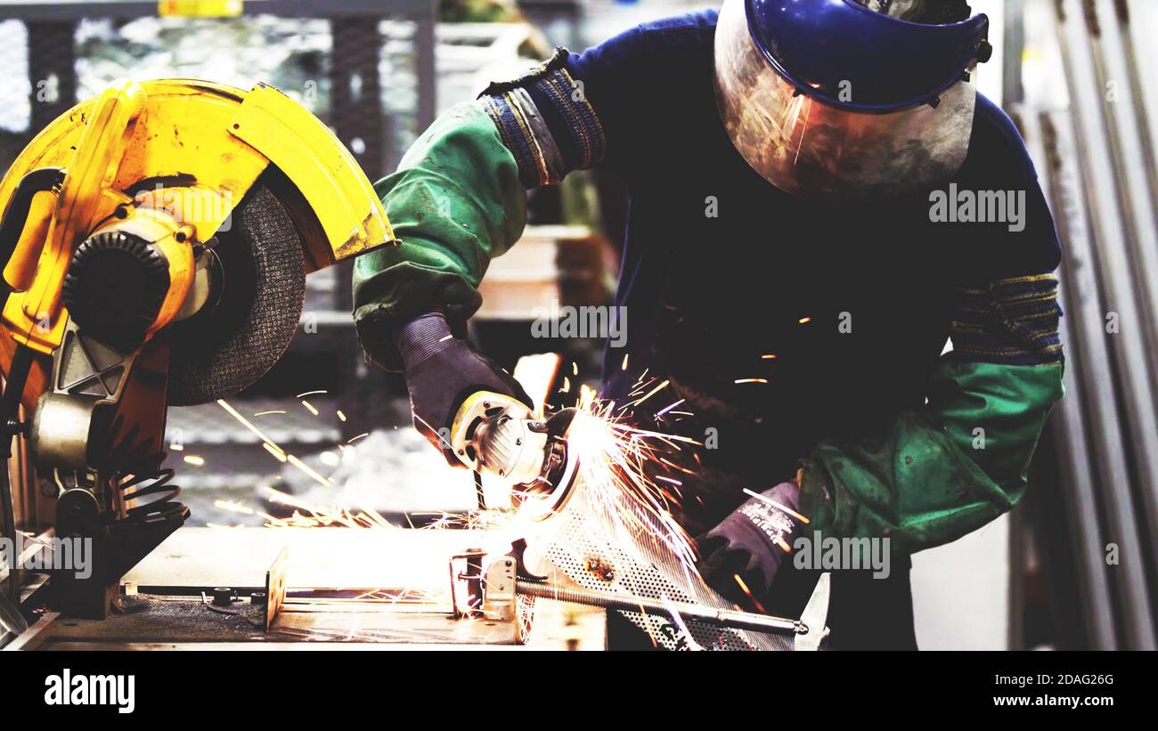 Schwere Industrie Arbeiter schneiden Stahl mit elektrischer Schleifmaschine in der industriellen Fabrikfertigung, tragen Sicherheitsausrüstung Stockfoto
