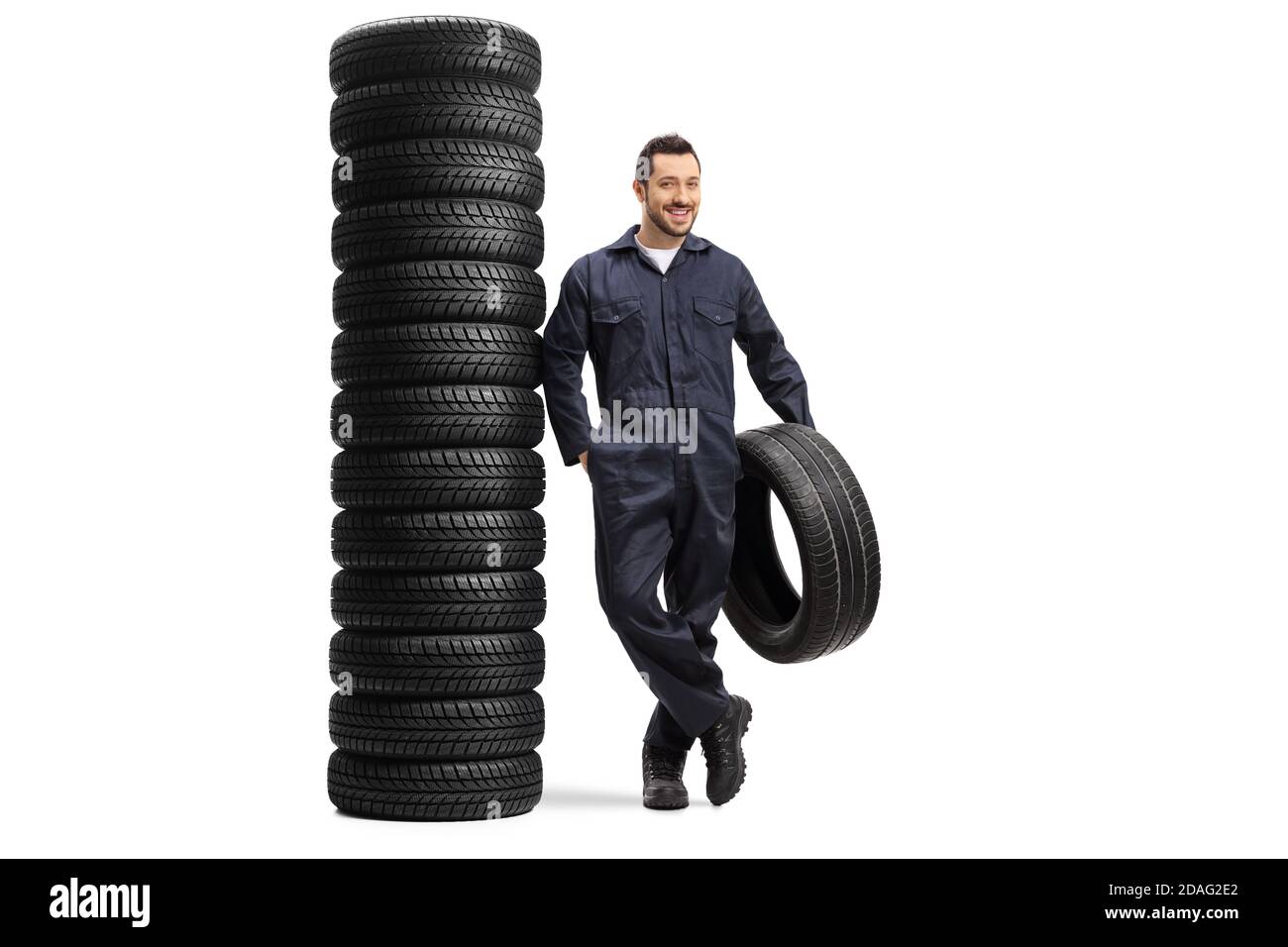Porträt eines Auto-Mechanikers, der einen Reifen hält Lehnt sich auf einen Haufen Autoreifen isoliert auf weiß Hintergrund Stockfoto