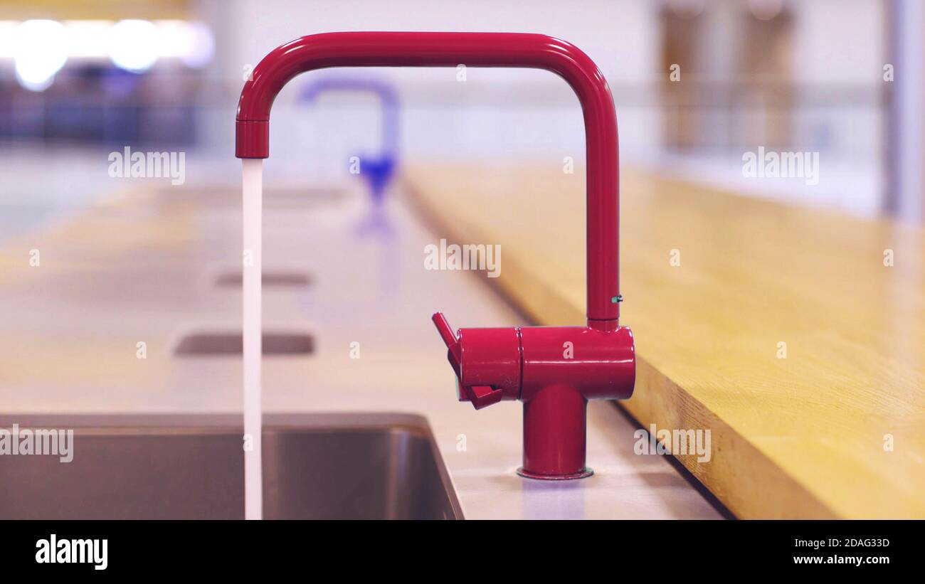 Roter Wasserhahn in der öffentlichen Küche, während Wasser aus ihm. Stockfoto
