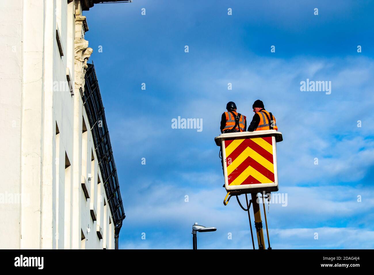 Zwei Männer, die in der Höhe in einem Kirschpflücker-Set arbeiten Vor einem frischen blauen Himmel Stockfoto