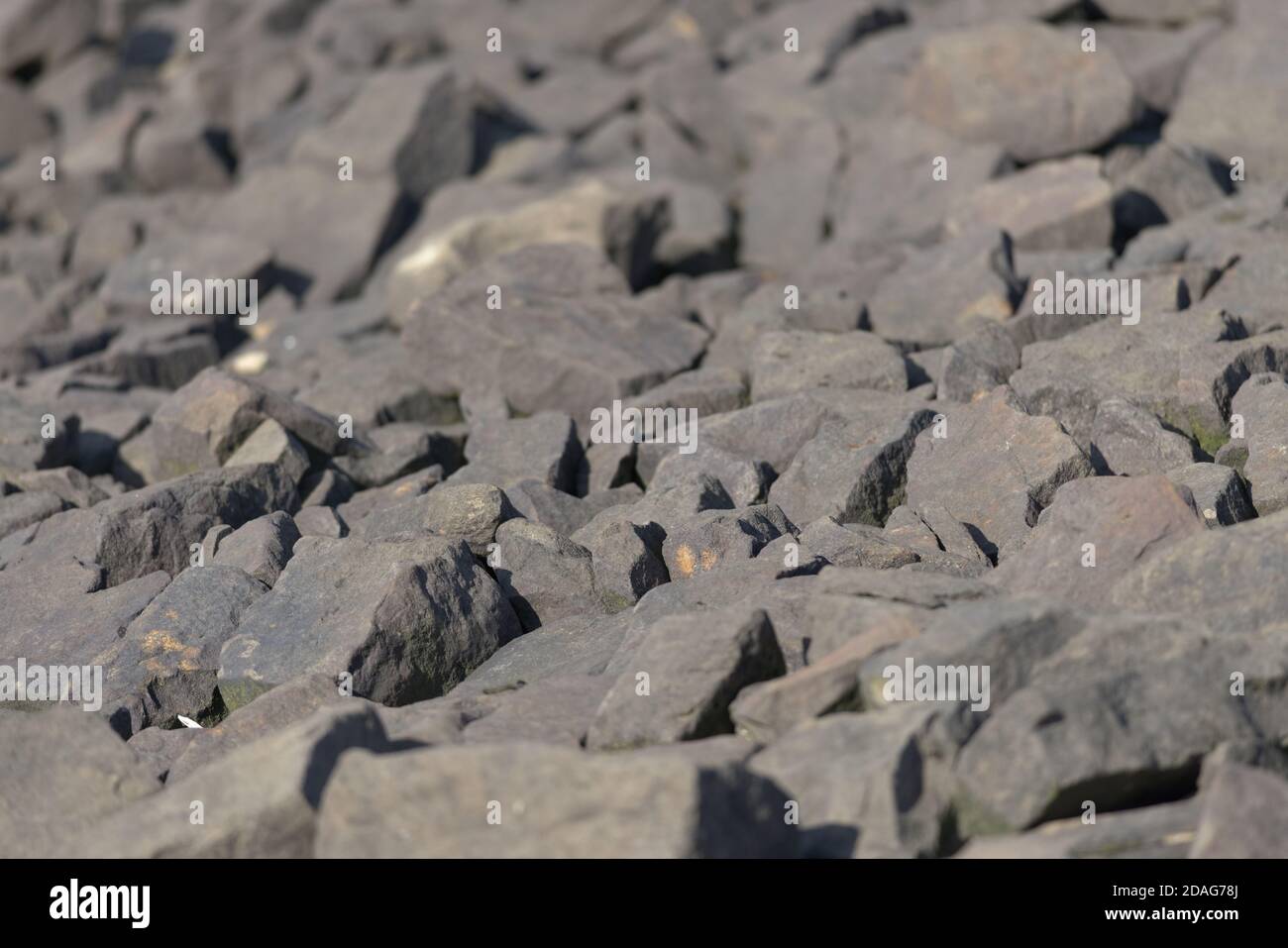 Verschiedene Größen der Steinbrocken vom Rand des Stausees bilden ein Bild des Vollbilds. Warme, klare Farbtöne von der Abendsonne. Natur im Freien Stockfoto