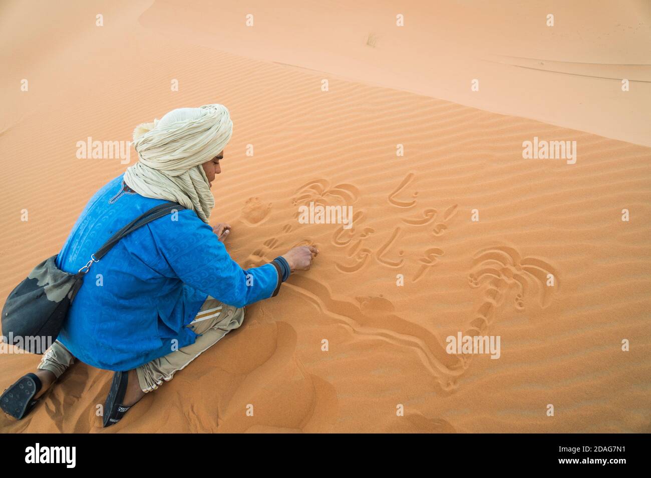 Merzouga, Marokko - APRIL 29 2019: Traditionell blau gekleidete marokkanische Zeichnung im Sand der Sahara Stockfoto