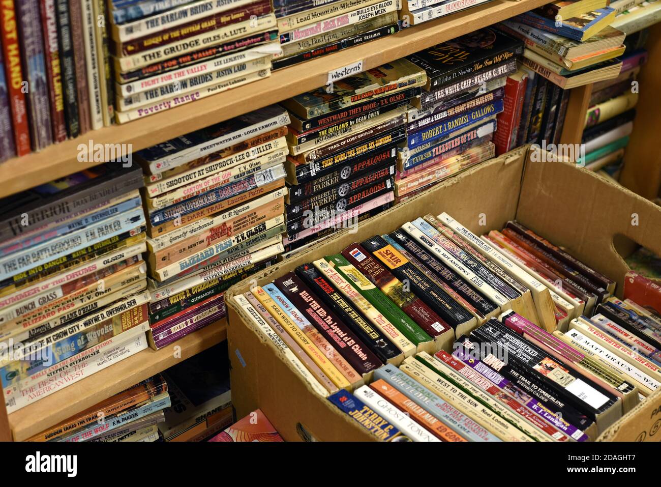Alte gebrauchte westliche Romane liegen auf einem Regal und in Eine Schachtel in einem gebrauchten Buchladen Stockfoto