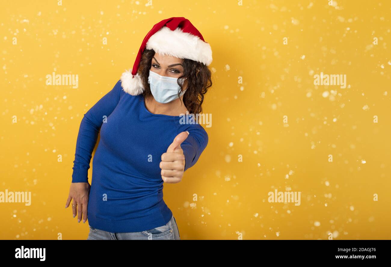 Frau mit Weihnachtshut ist optimistisch über die Niederlage der covid 19 Coronavirus. Gelber Hintergrund. Stockfoto