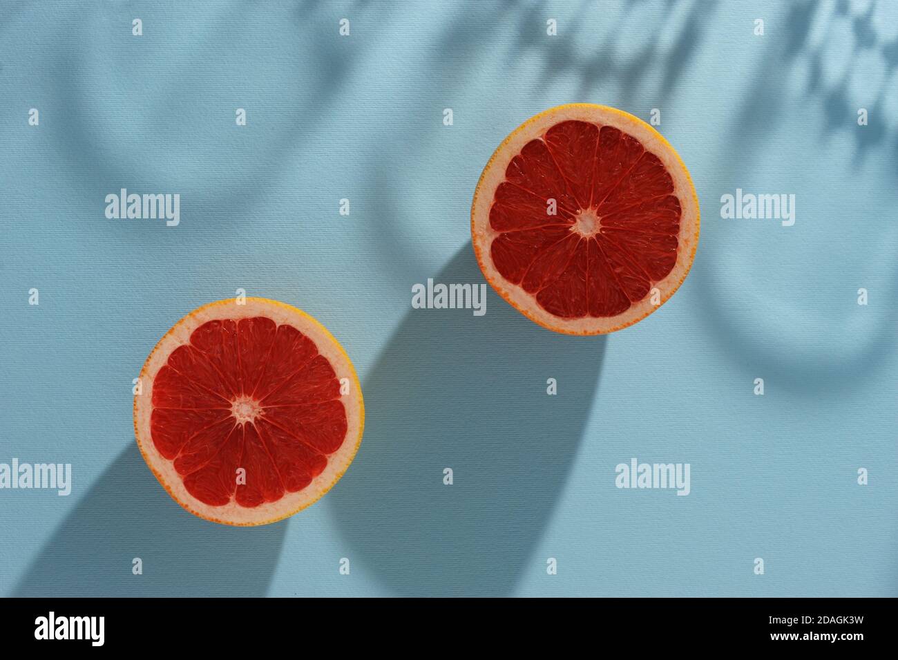 Kreativer Hintergrund mit zwei Scheiben Grapefruit und Schatten in minimalem Stil. Kreatives Layout für den Sommer. Horizontale Ausrichtung mit Platz für Text. Stockfoto