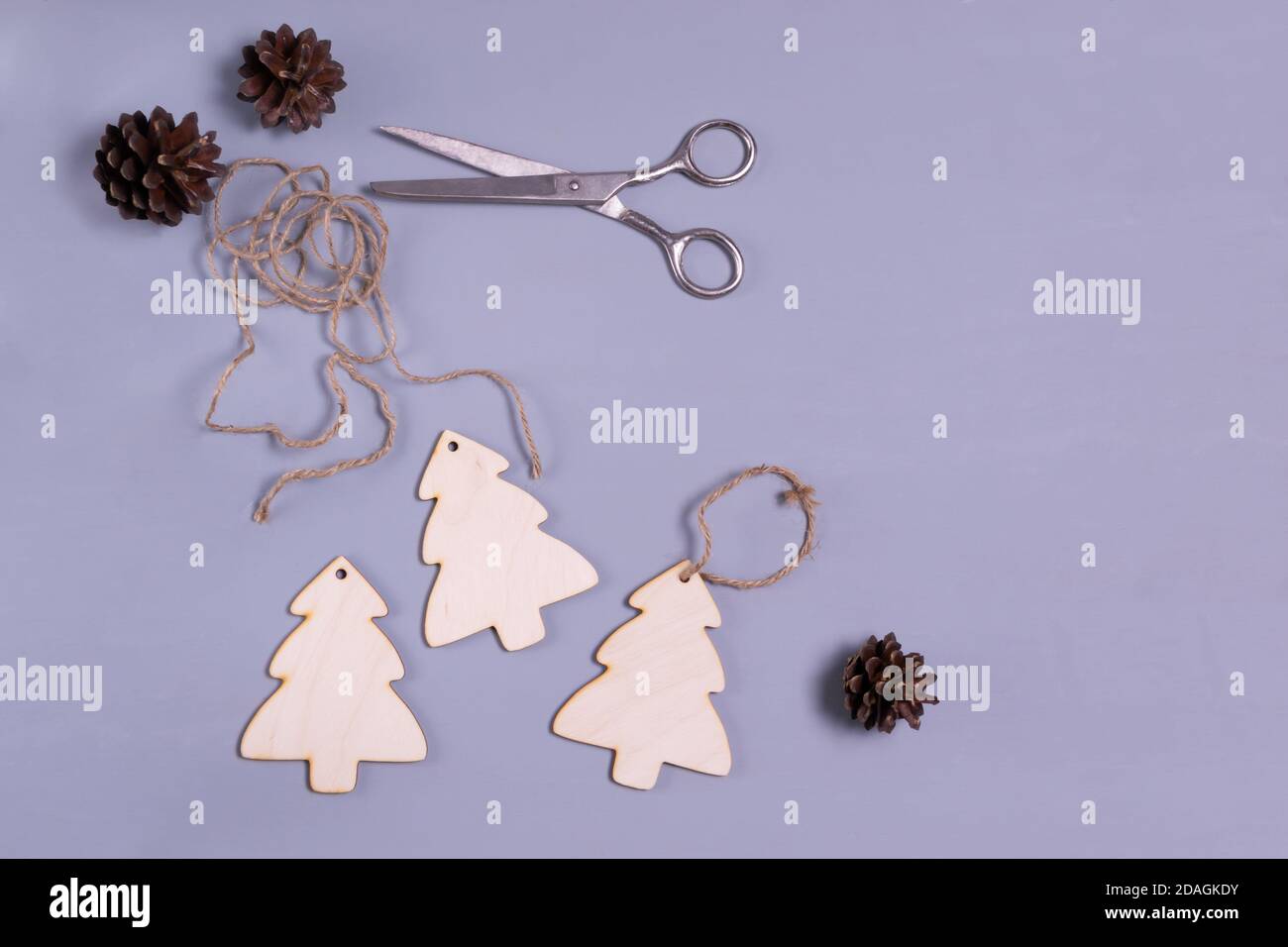 Weihnachtsbaumspielzeug aus Holz mit Schnur und Schere auf grauem Hintergrund. Natürliches Weihnachtsdekor-Konzept. Speicherplatz kopieren. Draufsicht. Stockfoto