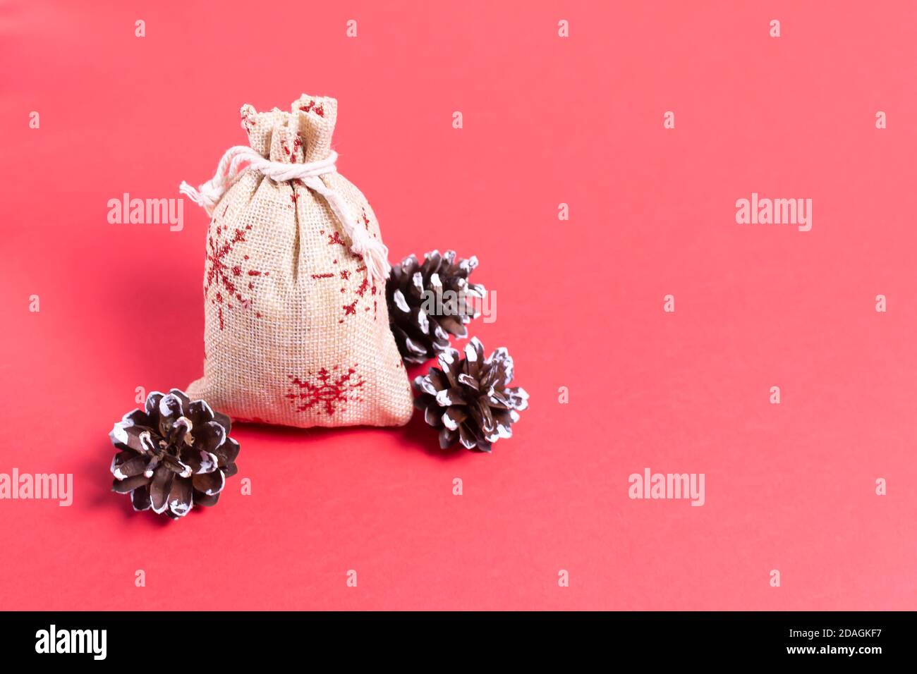 Natürliche Tasche mit Geschenken und Tannenzapfen auf rotem Hintergrund. Natürliches Weihnachtsdekor-Konzept. Speicherplatz kopieren. Stockfoto