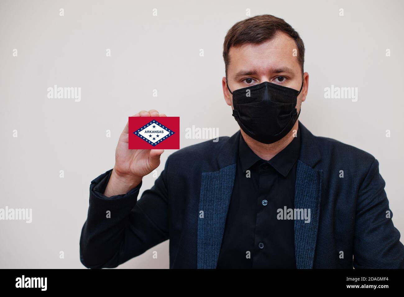 Mann tragen schwarz formell und schützen Gesichtsmaske, halten Arkansas Flagge Karte isoliert auf weißem Hintergrund. USA Coronavirus Covid Länderkonzept. Stockfoto