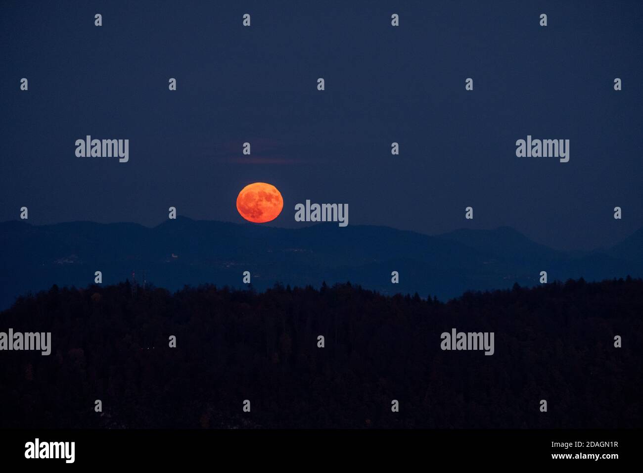 Riesiger oranger Vollmond, der in den Nachthimmel dahinter aufsteigt Ein Bergrücken mit Hügelschichten im Vordergrund Eine mystische Atmosphäre schaffen Stockfoto