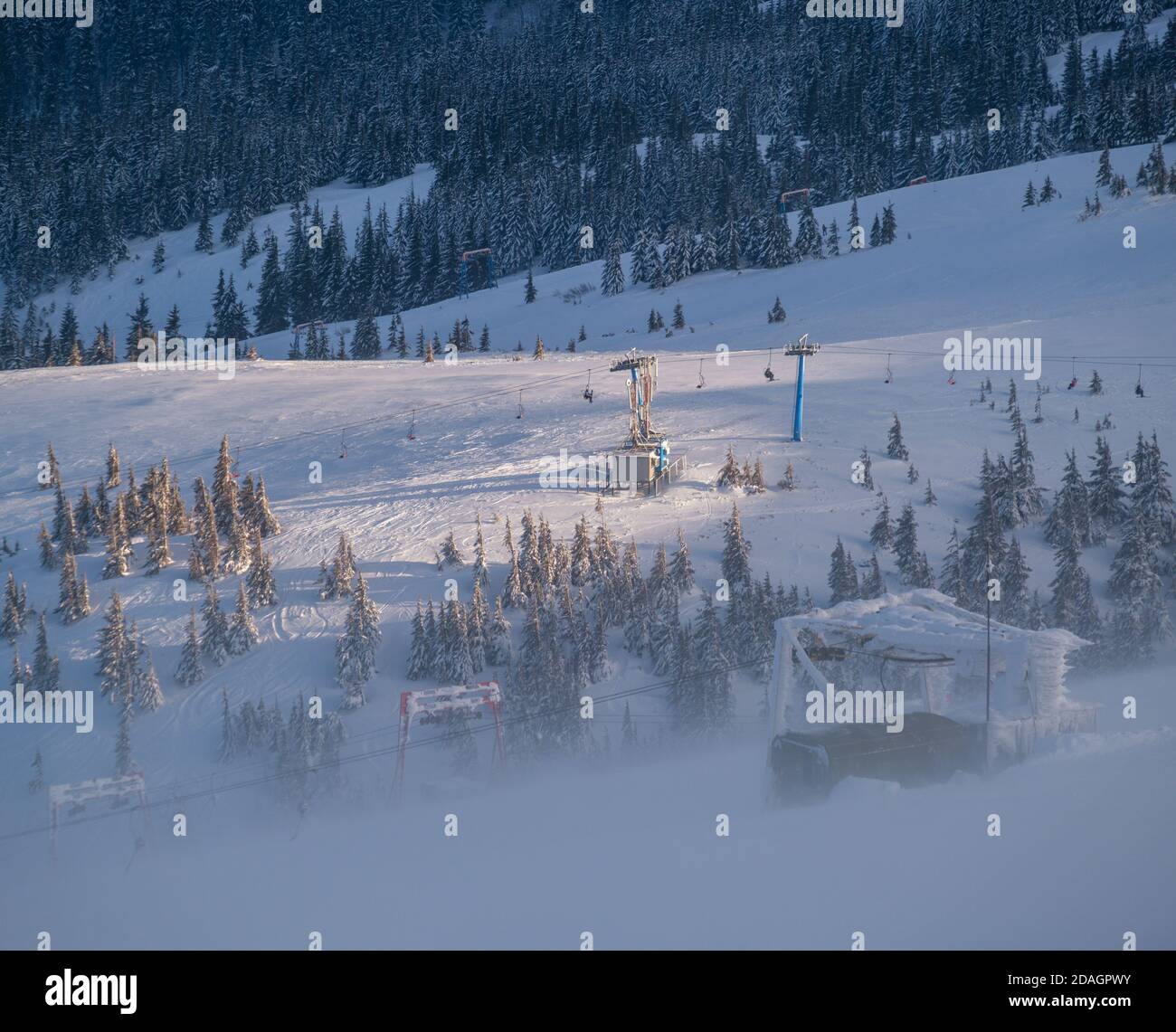 Alpine resortr Skilift mit Sitzen über den Sonnenuntergang Berg Skipisten bei extrem windigem Wetter. Menschen sind nicht erkennbar. Stockfoto