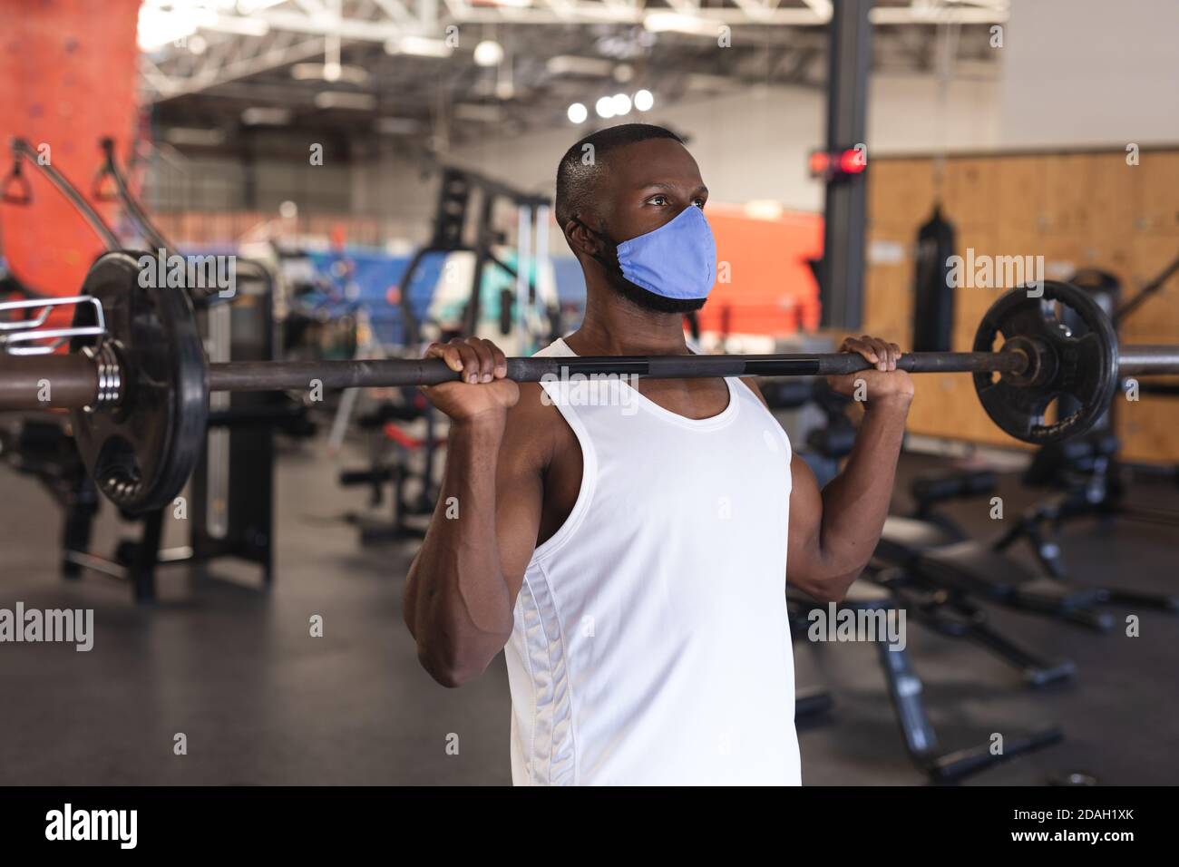 Fit afroamerikanischen Mann trägt Gesichtsmaske Durchführung Übung mit Langhantel im Fitnessraum Stockfoto