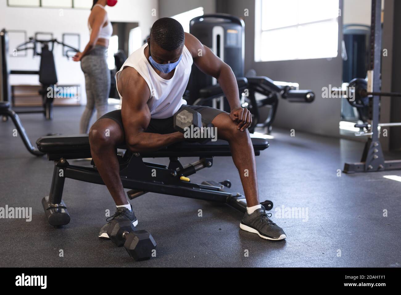 Fit afroamerikanischen Mann trägt Gesichtsmaske Durchführung Übung mit Kurzhantel im Fitnessstudio Stockfoto