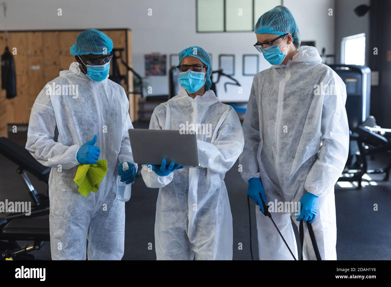 Team von Mitarbeitern tragen Schutzkleidung und Gesichtsmasken mit Laptop im Fitnessraum Stockfoto