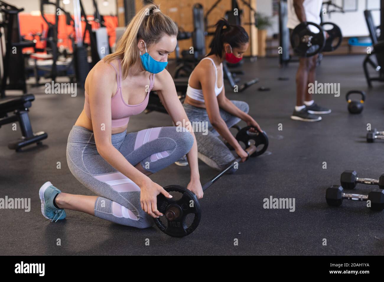 Zwei fit kaukasische Frau trägt Gesichtsmasken hinzufügen Gewichte in Langhantel im Fitnessraum Stockfoto