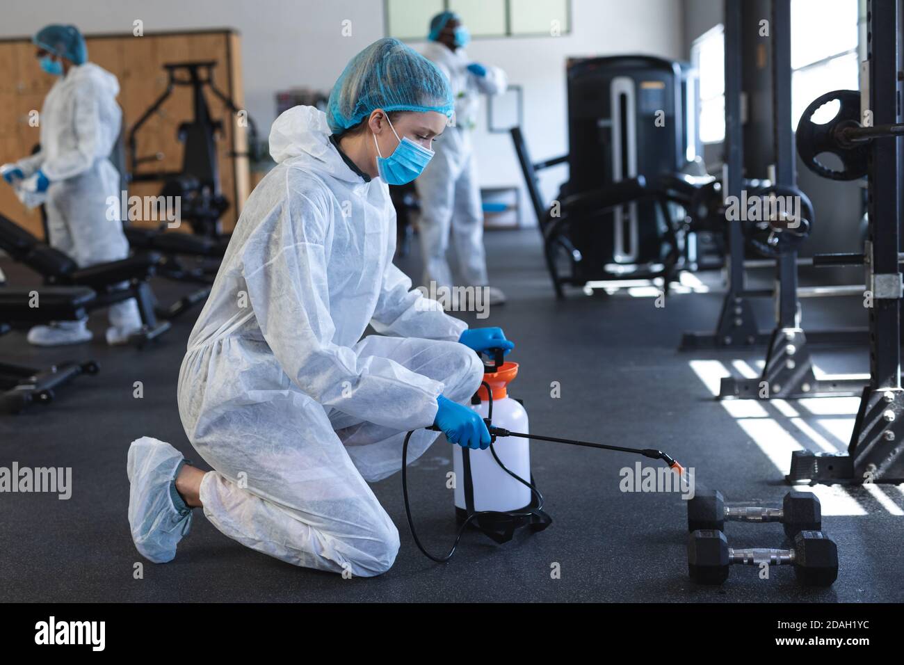Arbeiterinnen tragen Schutzkleidung und Gesichtsmasken Reinigung der Fitnessstudio mit Desinfektionsmittel Stockfoto