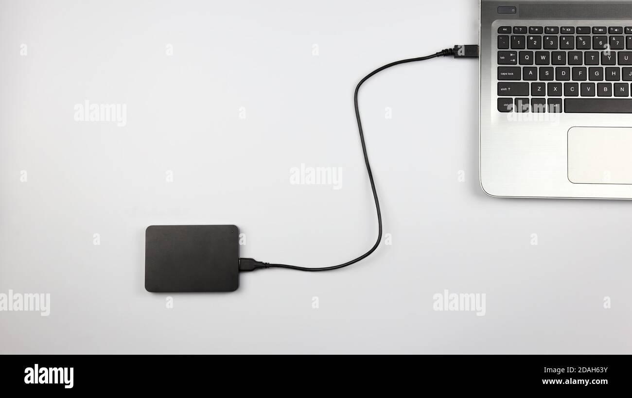 Externe Festplatte an Laptop auf weißer Oberfläche angeschlossen. Konzept für Büro, Wirtschaft, Bildung und Präsentation Stockfoto