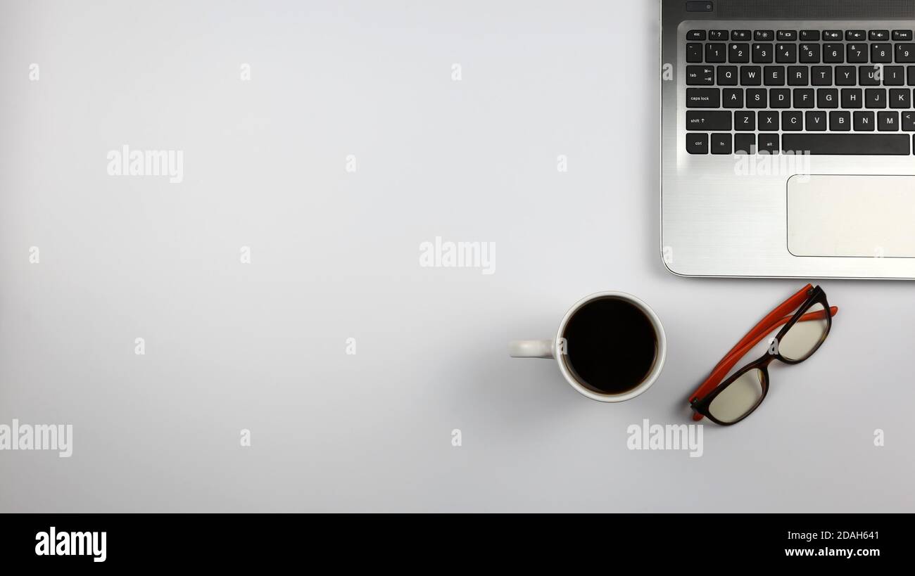 Schreibtisch mit Laptop, Gläsern und einer Tasse Kaffee auf weißer Oberfläche. Konzept für Büro, Wirtschaft, Bildung und Präsentation Stockfoto