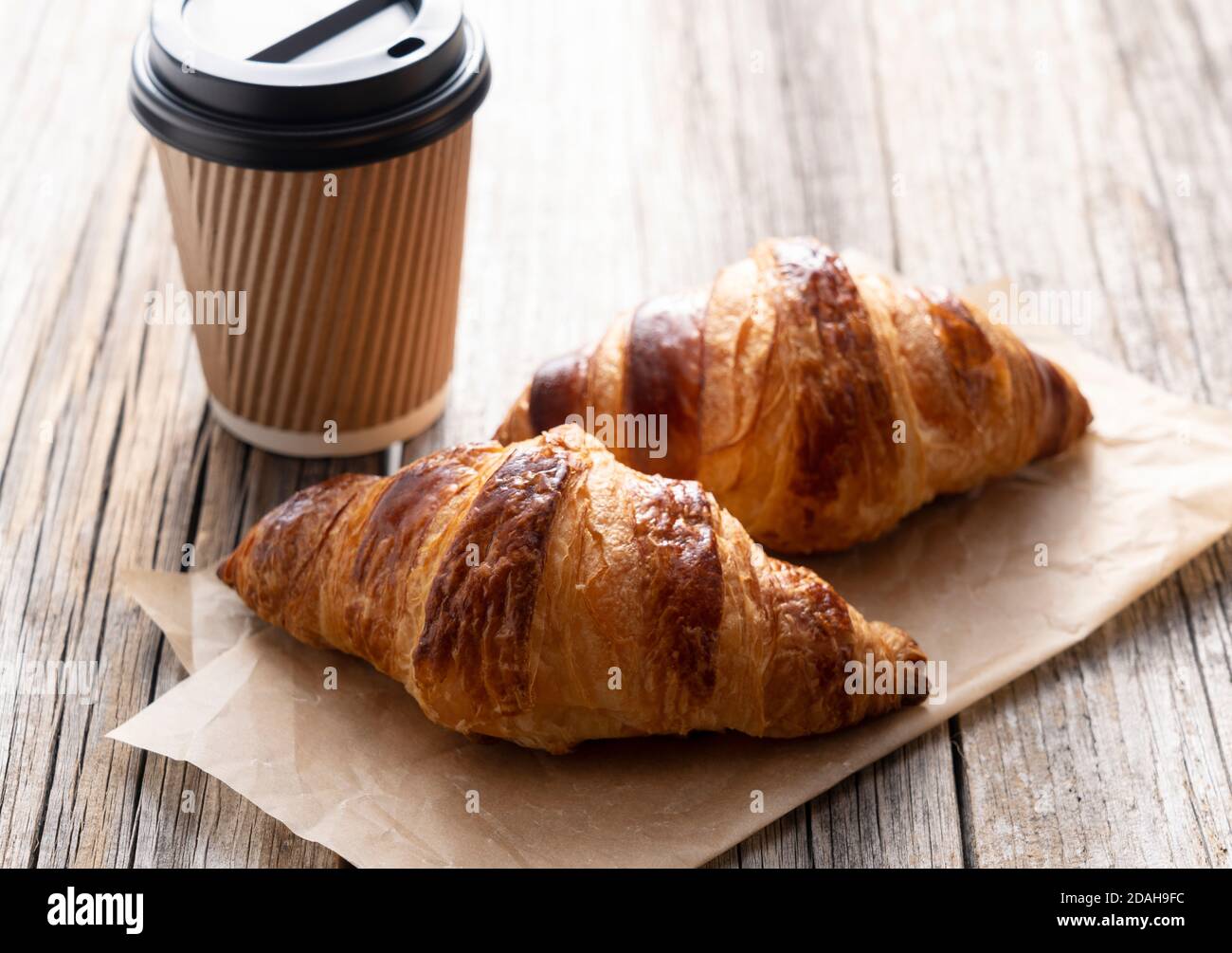 Croissants und Kaffee in einer Papiertasse auf einem alten Holzhintergrund. Bild Frühstück Stockfoto