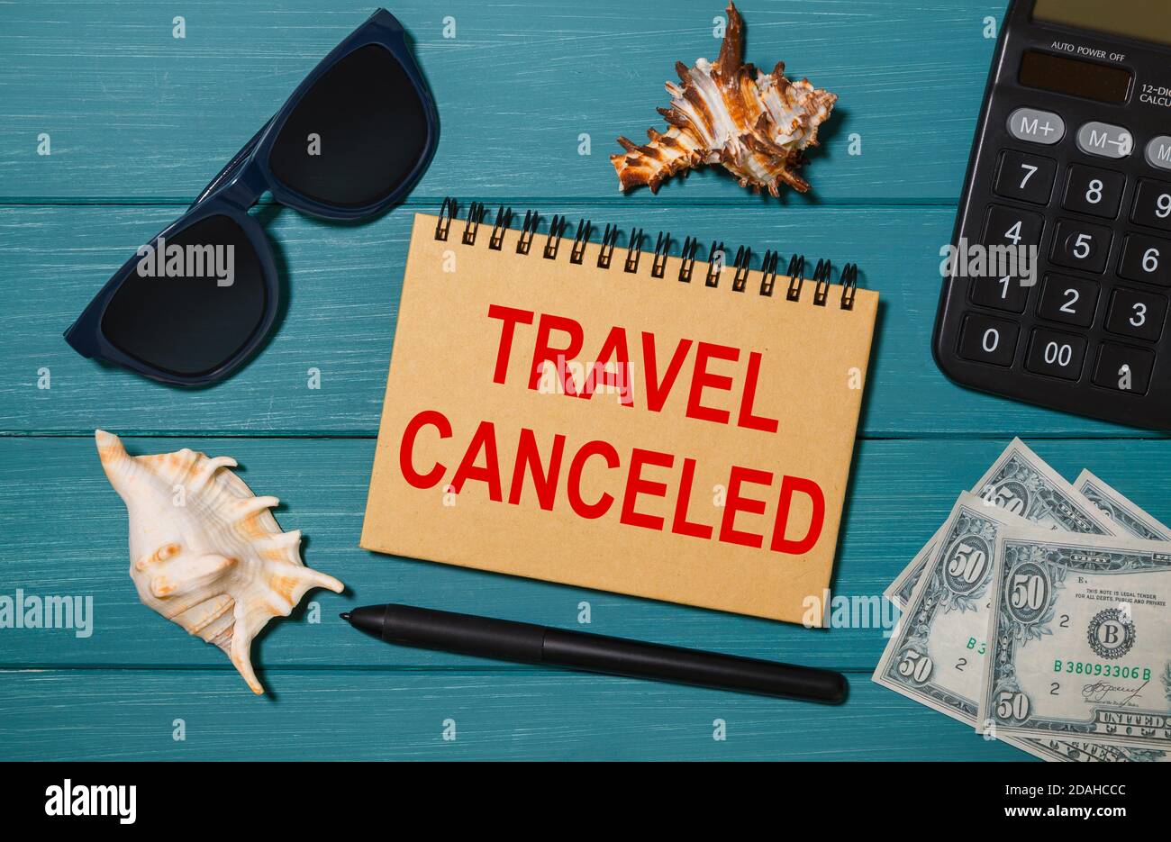 Bastelbuch mit den Worten Travel Cancelled, Brille, Geld, Taschenrechner und Muscheln Stockfoto