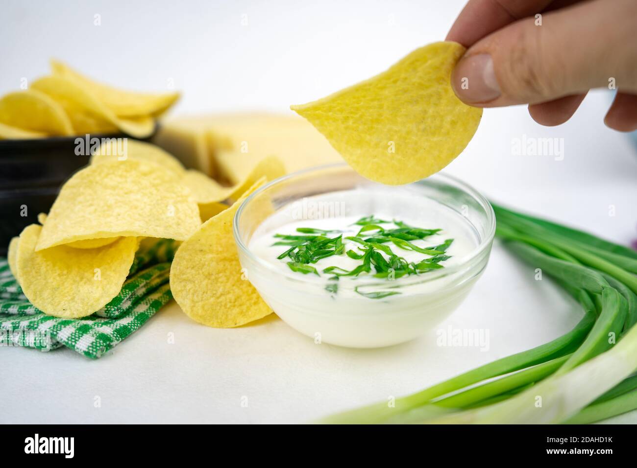 Nehmen Sie eine Chips aus einer Schüssel und tauchen Sie es in eine saure Sahne-Sauce mit grünen Zwiebeln. Stockfoto