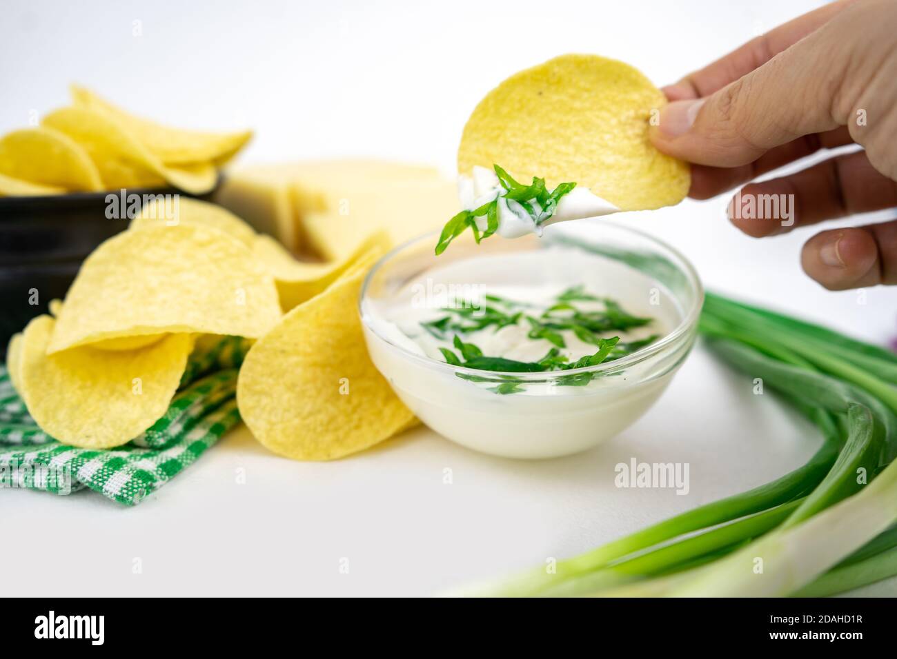Nehmen Sie eine Chips aus einer Schüssel und tauchen Sie es in eine saure Sahne-Sauce mit grünen Zwiebeln. Stockfoto