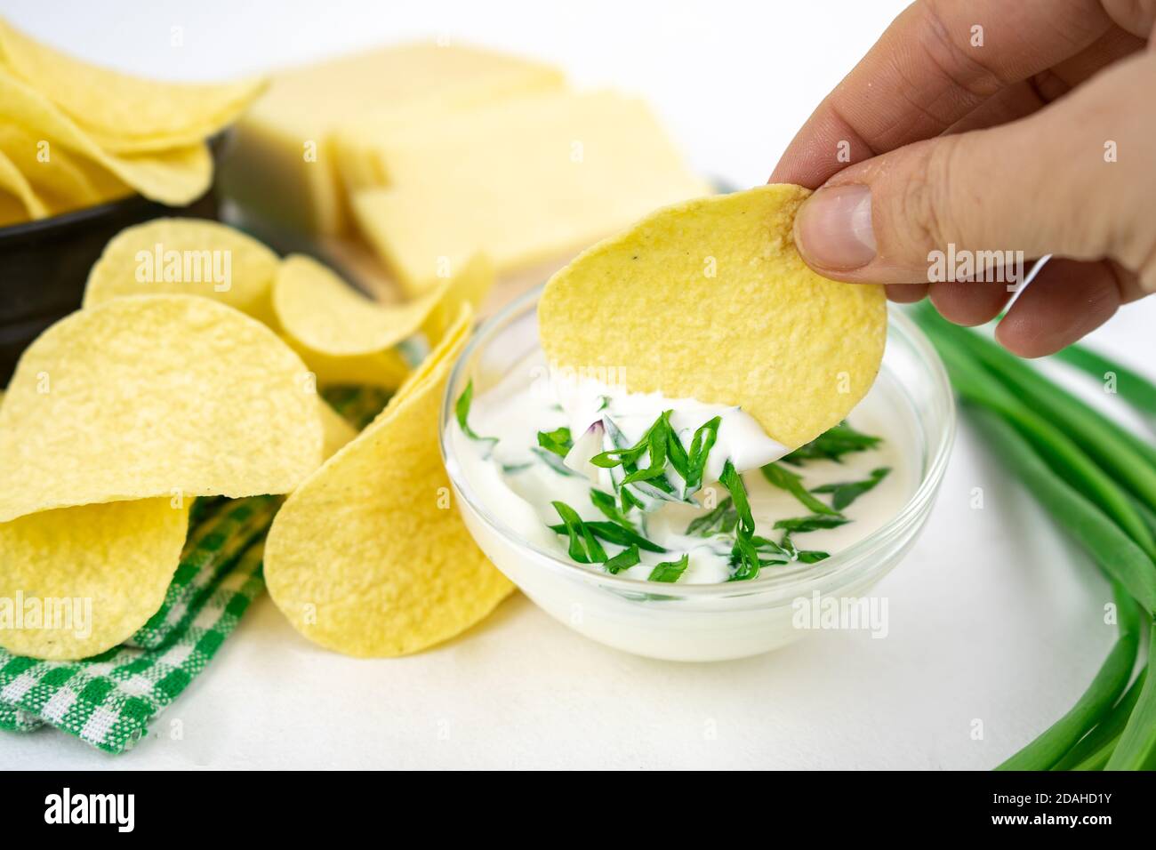 Nehmen Sie eine Chips aus einer Schüssel und tauchen Sie es in eine saure Sahne-Sauce mit grünen Zwiebeln. Stockfoto