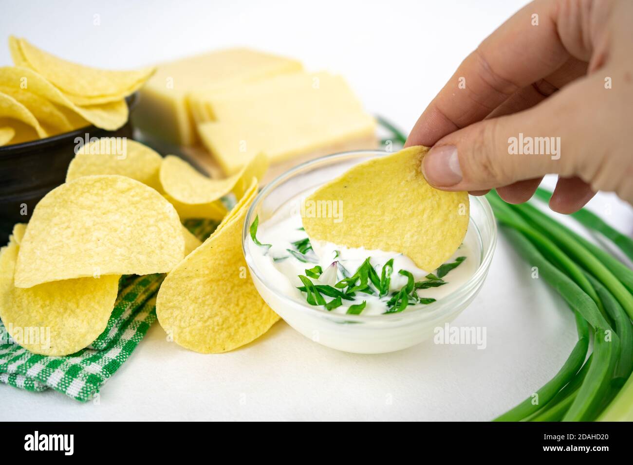 Nehmen Sie eine Chips aus einer Schüssel und tauchen Sie es in eine saure Sahne-Sauce mit grünen Zwiebeln. Stockfoto