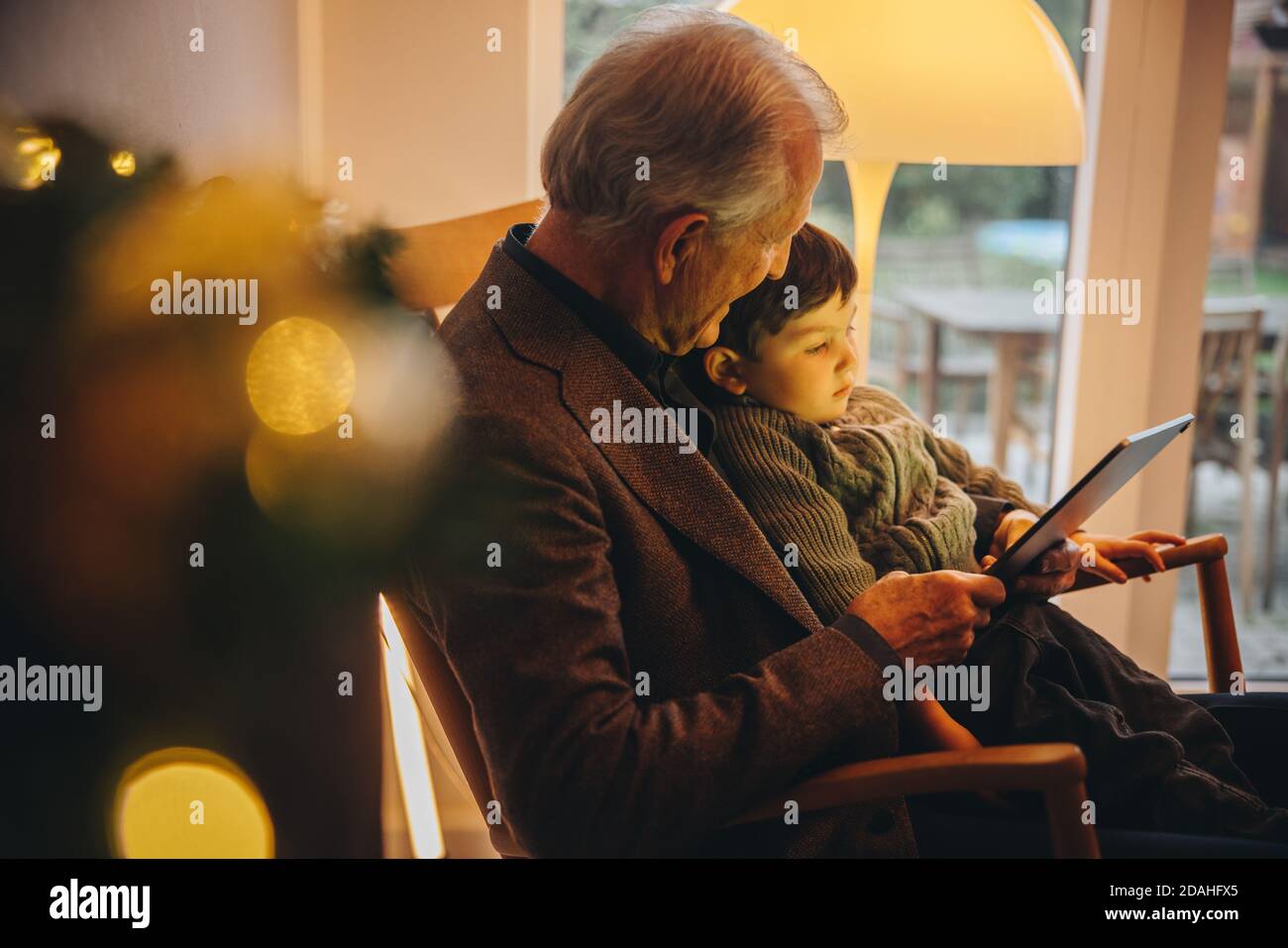 Älterer Mann mit ihrem Enkel, der einen Videoanruf auf einem digitalen Tablet hat. Großvater und Enkel sitzen auf einem Stuhl mit einem digitalen Tablet während der weihnachtszeit. Stockfoto