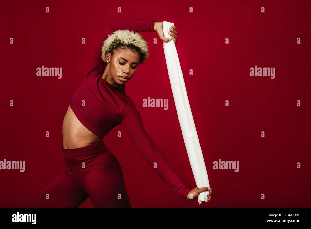 afroamerikanische Fitness-Frau, die mit einem Handtuch an Flexibilität arbeitet. Athletische Frau tut Fitness-Übung vor kastanienbraunen Hintergrund. Stockfoto