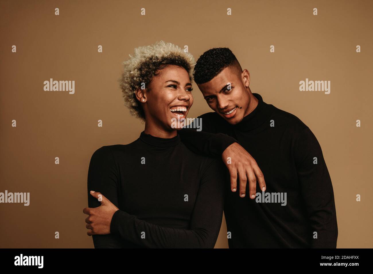 Glückliches Paar steht zusammen und lacht. afroamerikanischer Mann und Frau, die Spaß haben, vor braunem Hintergrund zu stehen. Stockfoto