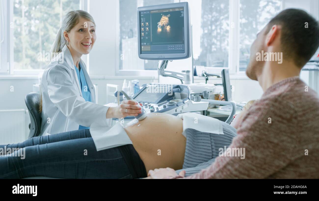 Im Krankenhaus, schwangere Frau bekommen Ultraschall-Sonogramm-Scan, Geburtshilfe erklärt ihr und ihrem unterstützenden Ehemann Verfahren. Frohe Familie Stockfoto
