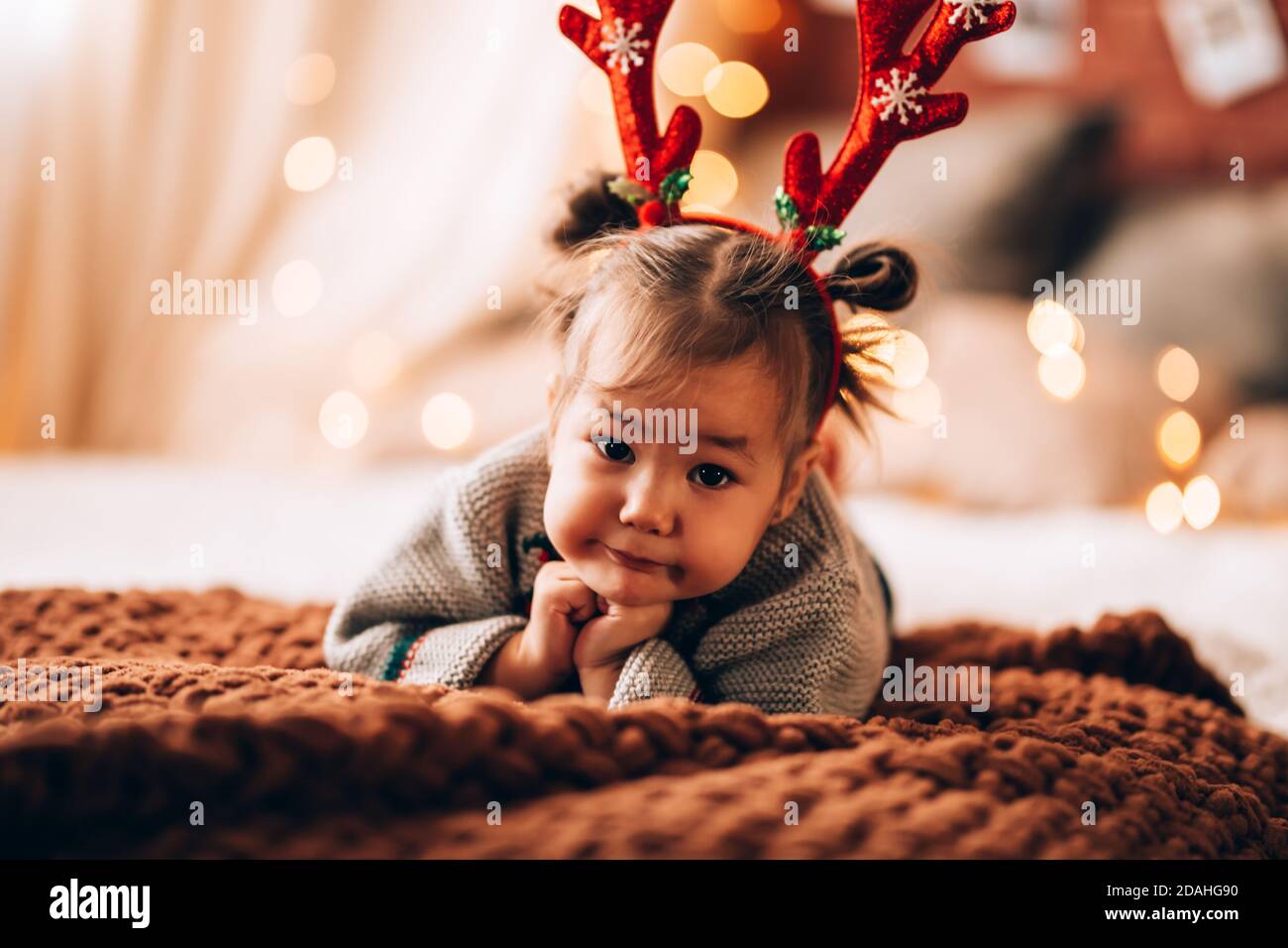 Kleines Mädchen liegt auf einem großen Bett. Das Kind hat Geweihe auf dem Kopf. Weihnachtsstimmung. Stockfoto