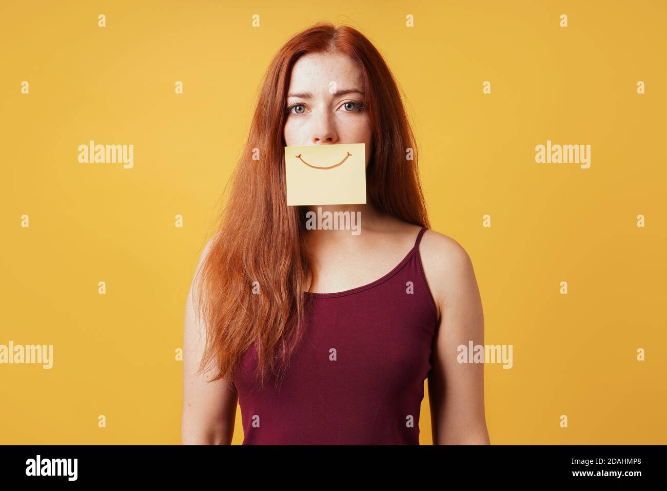 Junge Frau versteckt Traurigkeit oder Depression hinter gefälschten Lächeln gezeichnet Auf gelbem Notizpapier Stockfoto
