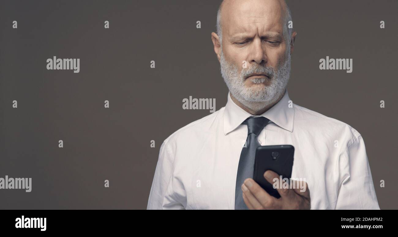 Mann mittleren Alters mit Schwierigkeiten und Sehstörungen mit seinem Smartphone ist er nicht in der Lage, kleine Texte auf dem Bildschirm zu lesen Stockfoto