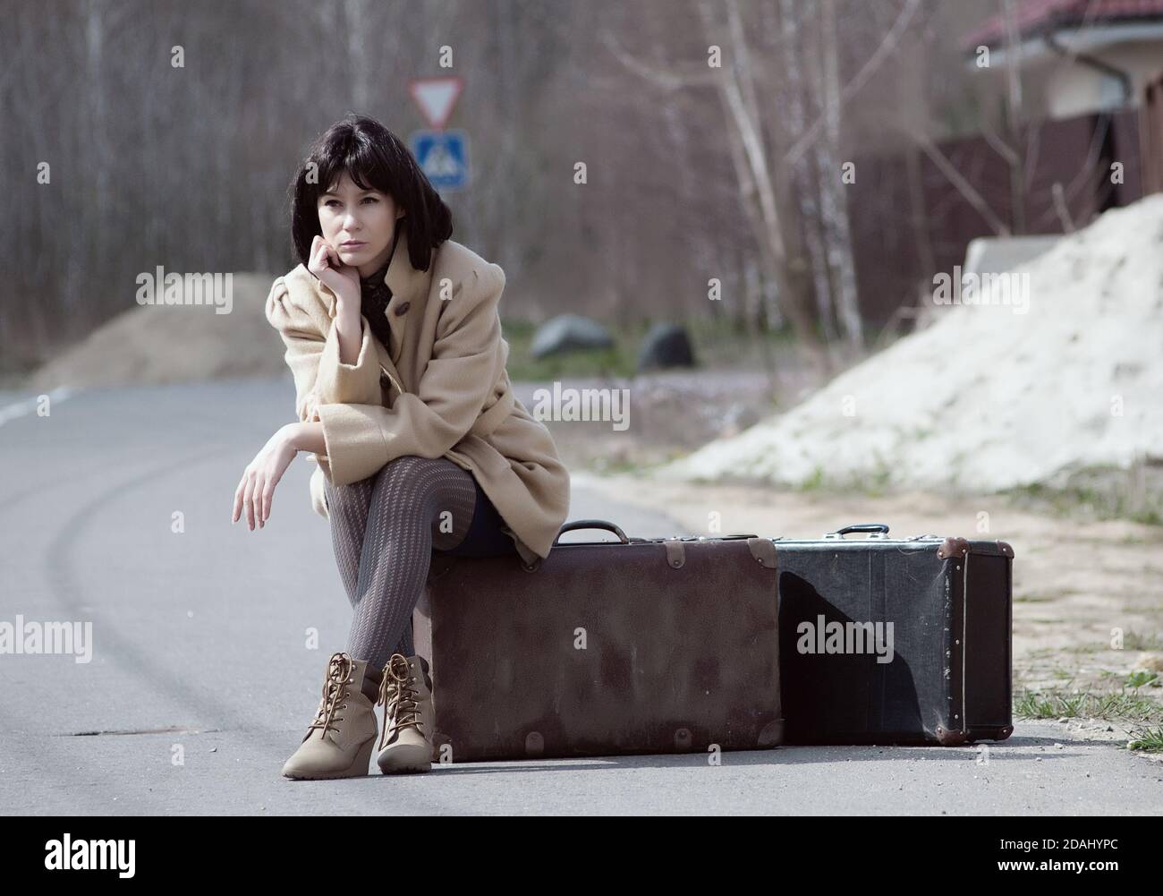 Brunette Frau wartet auf sitzen auf einem Koffer Stockfoto