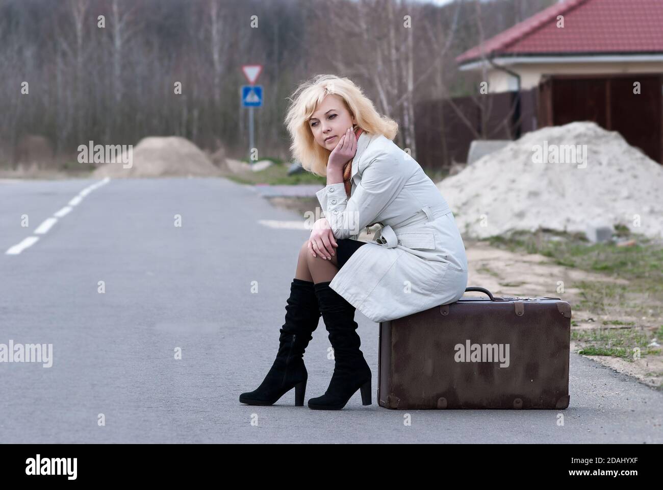 Blonde Frau wartet auf einem Koffer sitzen Stockfoto