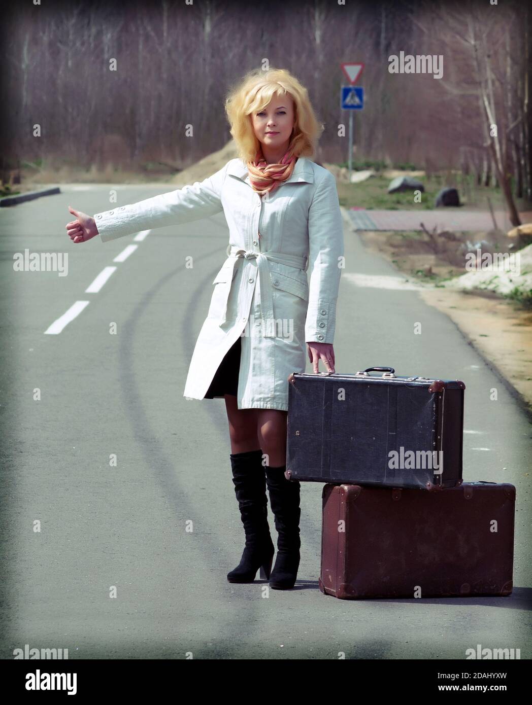 Blonde Mädchen stehen auf der Straße mit einem Koffer und Hitchhiking Shows Stockfoto