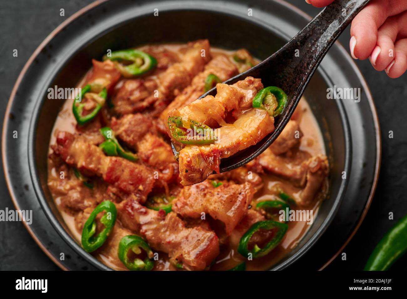 Bicol Express Eintopf in schwarzer Schale auf dunkler Schieferplatte. Philippinische Küche würziges Schweinebauch Kokosmilch-Curry. Asiatische Küche. Stockfoto